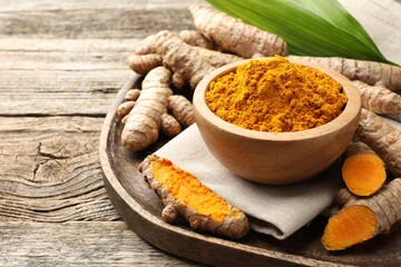 Turmeric powder in bowl and roots on wooden table, space for text