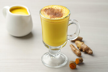 Delicious turmeric latte and rhizomes on white wooden table, closeup