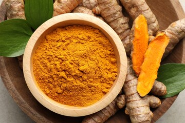 Aromatic turmeric powder in bowl, fresh roots and leaves on light grey table, top view