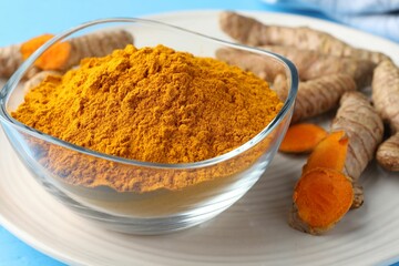 Aromatic turmeric powder in bowl and fresh roots on light blue table, closeup