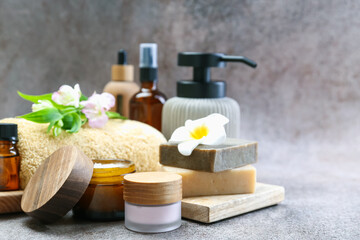 Different body care products and flowers on grey table, closeup