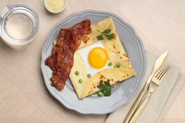 Delicious crepe with egg, bacon and green peas served on wooden table, flat lay. Breton galette