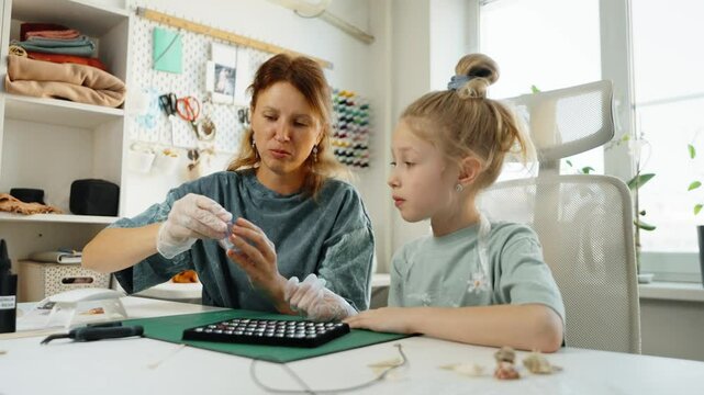 Family crafting activity, mother teaches daughter UF resin art. Hands carefully mix and pour resin, forming miniature jewelry pieces. Educational hobby fostering creativity and skill development.