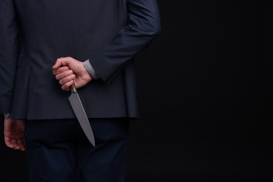 Businessman holding knife behind his back on black background, closeup. Space for text