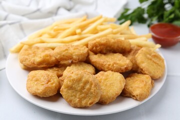 Tasty chicken nuggets and french fries with sauce on white tiled table, closeup