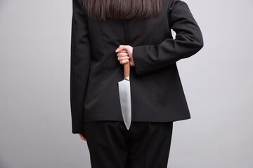 Businesswoman with knife behind her back on light grey background, closeup
