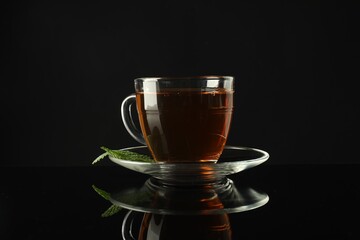 Aromatic tea in glass cup and mint on dark mirror table
