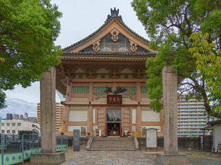 Fototapeta premium Osaka, Japan - Sep 21 2024, panoramic view of the building in cemetery an grounds of Shitennoji temple, with trees on a background and cloudy sky, without people, Osaka, Japan