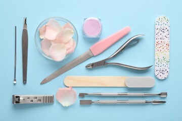 Set of different manicure tools and petals on light blue background, flat lay