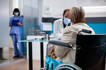 Obraz premium Senior woman in wheelchair sharing her medical concerns with young doctor during clinic visit. Female pensioner patient receiving detailed advice about her health from male physician in hospital room.
