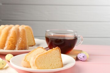 Pieces of delicious bundt cake, Easter eggs and tea on pink wooden table, closeup