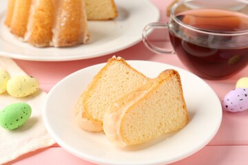 Pieces of delicious bundt cake, Easter eggs and tea on pink wooden table, closeup