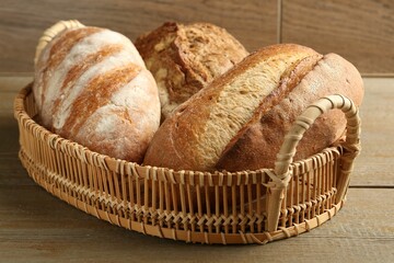 Different types of fresh bread in wicker basket on wooden table, closeup