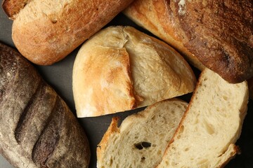 Different types of fresh bread on dark textured table, flat lay
