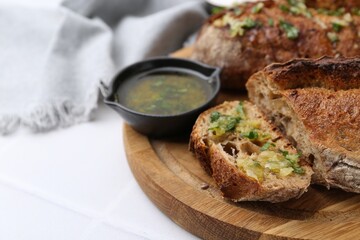 Tasty bread with garlic, herbs and oil on white tiled table, closeup. Space for text