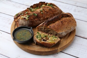 Tasty bread with garlic, herbs and oil on white wooden table, closeup