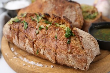 Tasty bread with garlic, herbs and oil on white table, closeup
