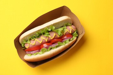 Tasty hot dog with tomato, onion, lettuce and mustard on yellow background, top view