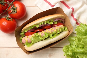 Tasty hot dog with tomatoes, onion, lettuce and mustard on wooden table, flat lay