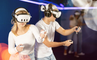 Girl with guy pair wearing virtual reality glasses participate in game with opponents. They compete two-on-two with friends while playing in parallel virtual world..