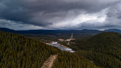 Dramatic sky over pine forest and frozen lake in mountain valley