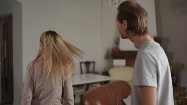 A blonde woman waves a bundle of cash in front of her partner s face, then turns and walks away. He looks angry and shouts in frustration, showing signs of stress. The scene is set indoors in a cozy