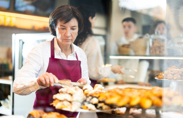 Naklejka premium Elderly woman seller putting fresh pastries on plate in cafe bakery