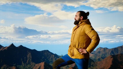 Hiker pauses to admire the panoramic mountain scenery on the hill top, endless sky and rugged peaks...