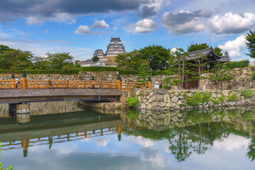 Himeji, Japan - Sep 24 2024, panoramic view of pond, bridge in front of fortress wall with gates of Himeji Castle, White Heron Castle, with castle itself in background, at daytime, Himeji, Japan