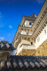 Himeji, Japan - Sep 24 2024, vertical, panoramic view of Himeji Castle, White Heron Castle from behind the roof of the castle outbuildings, in the daytime with blue sky, without people, Himeji, Japan