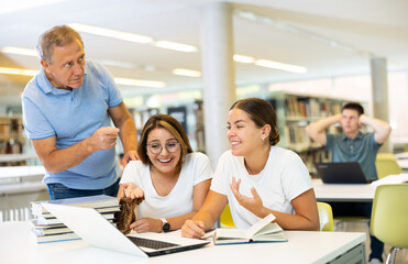 Fototapeta premium Mature annoyed male interrupts noisy female students laughing in the library..
