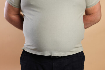 Overweight man in tight t-shirt on beige background, closeup