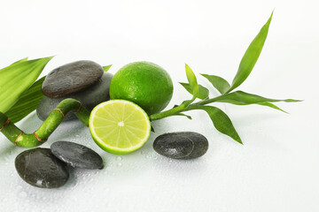 Spa composition with limes, massage stones and bamboo stem on wet surface