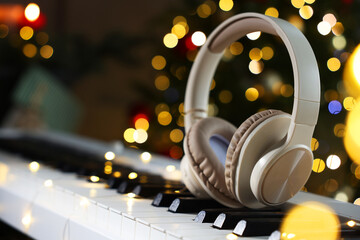 Headphones on electric piano against Christmas tree with blurred lights, closeup. Bokeh effect
