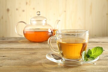 Freshly brewed tea in glass cup and teapot on wooden table