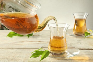 Pouring freshly brewed tea from teapot into glass cup on wooden table, closeup