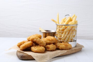 Tasty chicken nuggets, potato fries and sauce on white tiled table, closeup