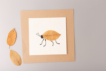 Handmade insect artwork using autumn leaves and drawing on paper. Flat lay composition on grey background. Creative autumn craft and DIY art concept for handmade product promotion, school projects,