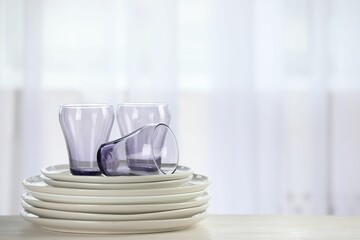 Empty clean glasses and plates on table indoors, space for text