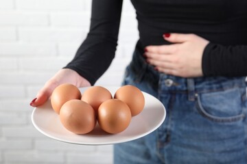 Woman refusing to eat eggs near white brick wall, closeup. Food allergy concept