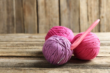 Balls of colorful yarn and crochet hook on wooden table, closeup. Space for text