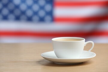 Cup of coffee on wooden table against American flag. Space for text