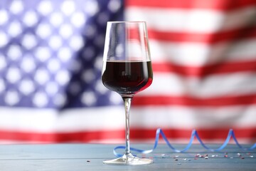 Glass of wine and party streamers on blue wooden table against American flag