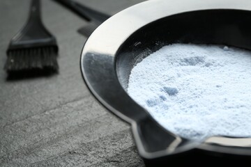 Bowl with hair bleaching powder and brush on black table, closeup