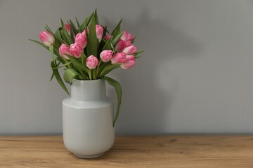 Bouquet of beautiful tulips in vase on wooden table against light grey background, space for text