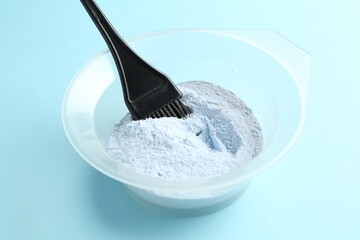 Bowl with hair bleaching powder and brush on light blue background, closeup
