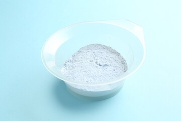 Bowl with hair bleaching powder on light blue background, closeup