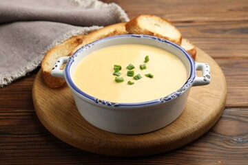 Tasty cheese dipping sauce in bowl and croutons on wooden table, closeup