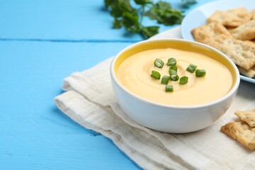 Tasty cheese dipping sauce in bowl and crackers on light blue wooden table, closeup. Space for text