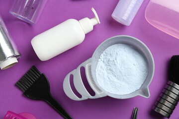 Bowl of hair bleaching powder and hairdresser's tools on purple background, flat lay